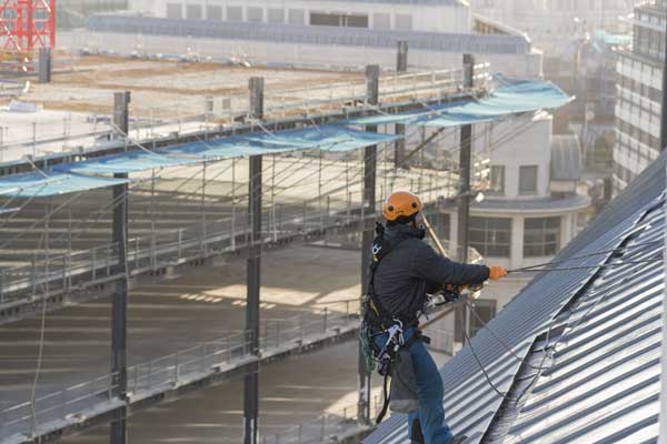Man in safety equipement working on a sloping roof-top.