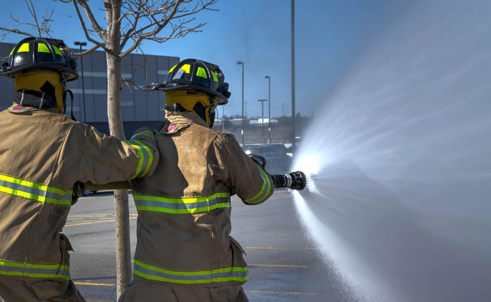 Two fire fighters in an office car park using the fire hose