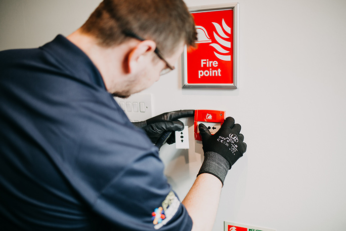 A PTSF Neo fire technician working on a wall-mounted fire alarm