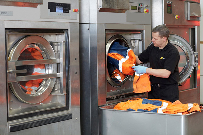 A phs Besafe employee putting PPE into an industrial washing machine