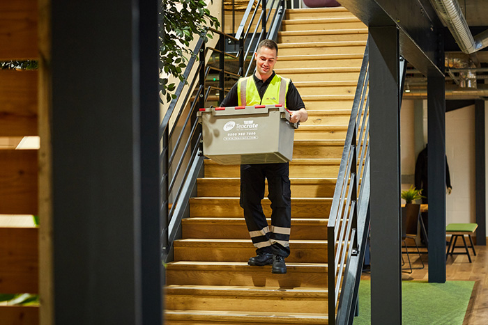 An office mover carrying a phs Teacrate storage box down a flight of stairs