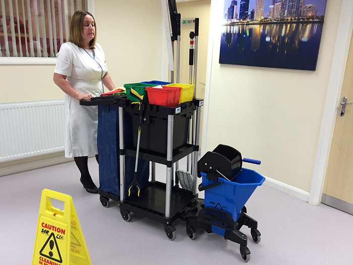 A cleaner with a trolley full of equipment and products