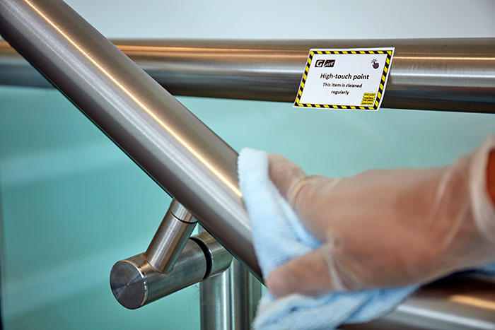 A cleaner sanitising a stair handrail